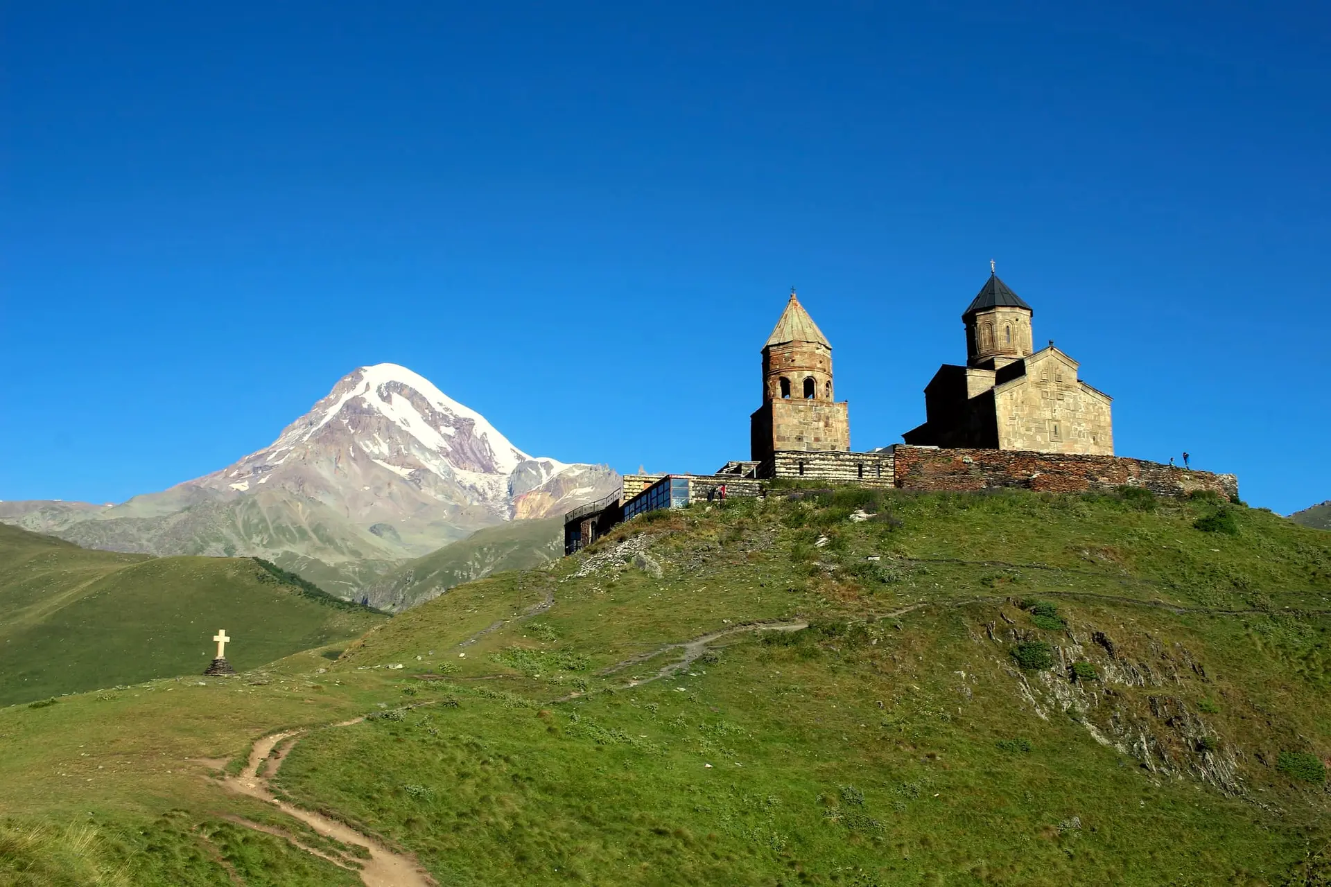 Gergeti Trinity Church and its bell tower on a green hill, with snowy Mount Kazbek behind