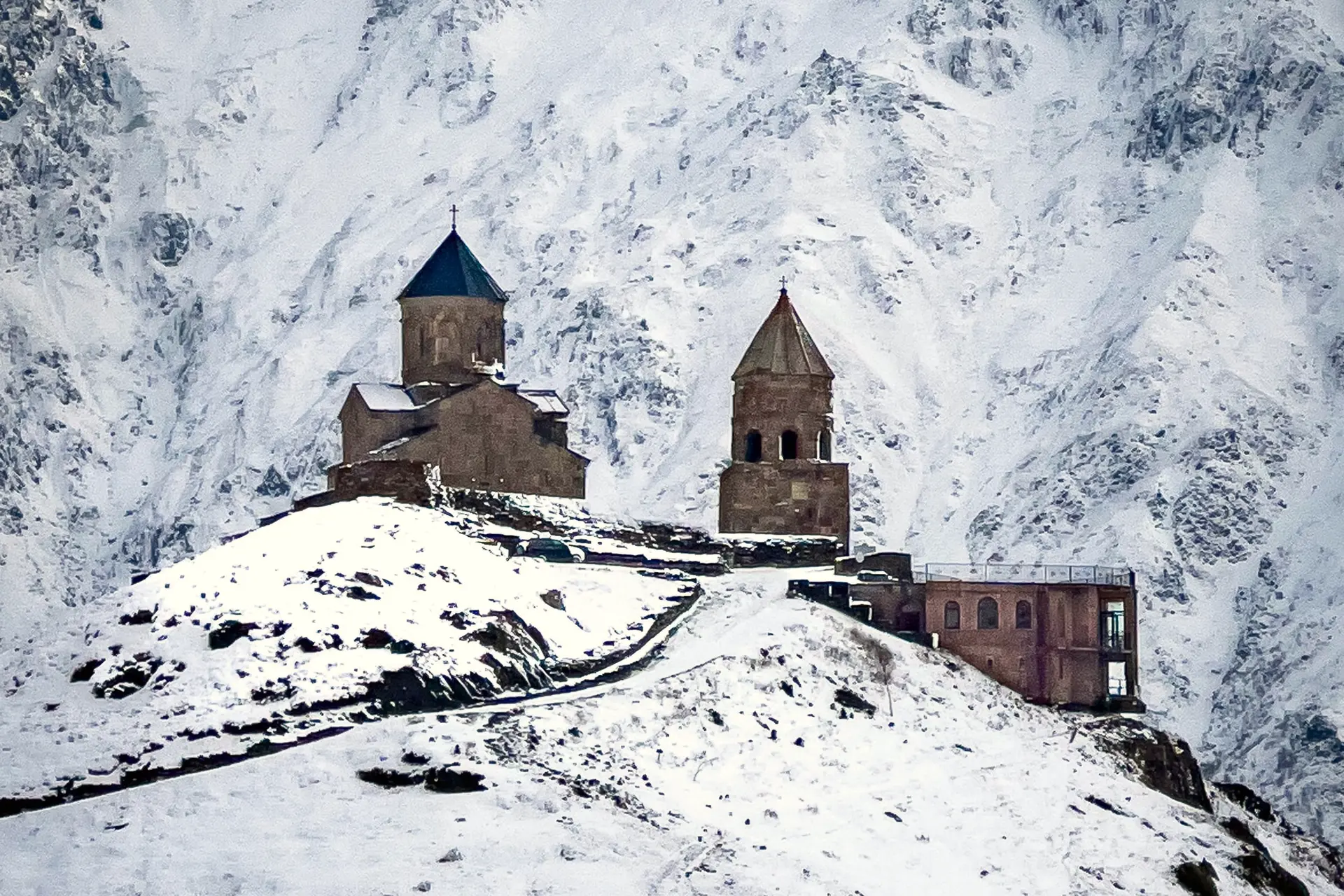 Gergeti Trinity Church on its snow-covered hill, with snowy mountains behind