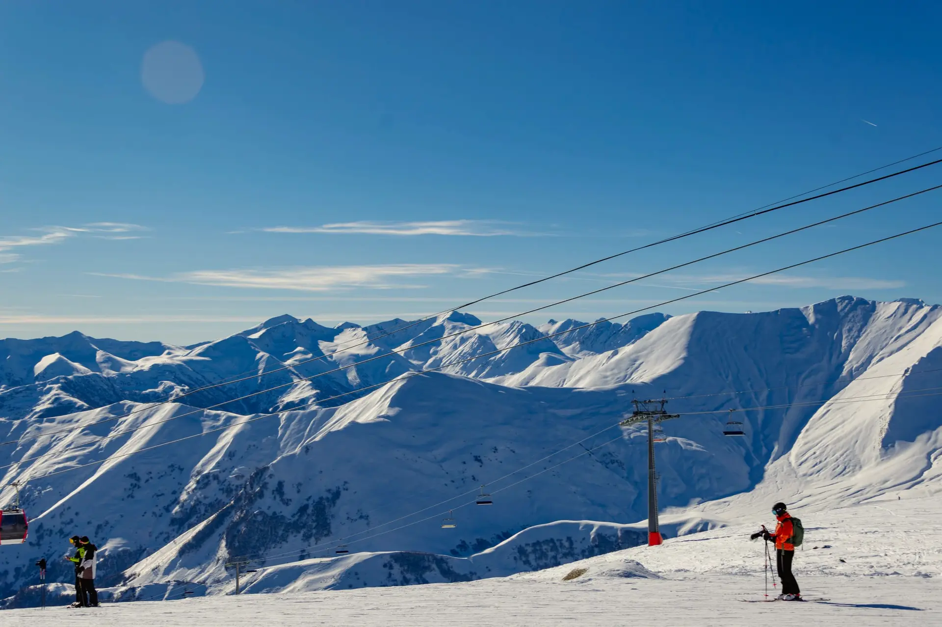 Skiers on a wide groomed slope under the snowy peaks of the Caucasus