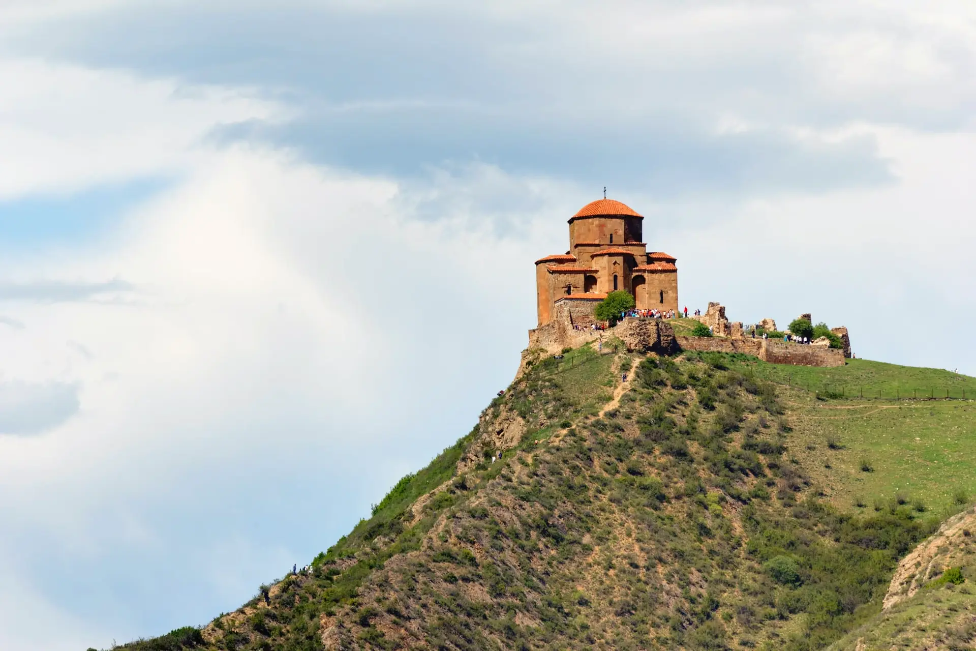 Jvari Monastery on a green hilltop above Mtskheta, with visitors by its old walls