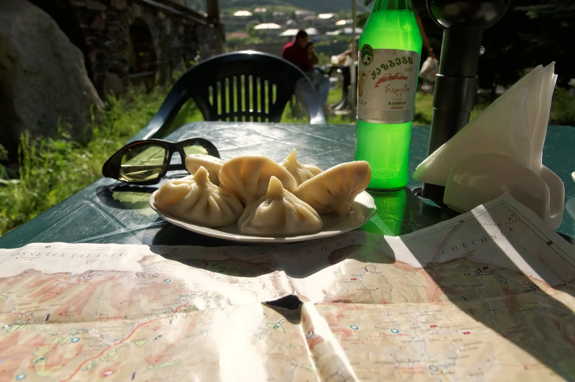 A plate of khinkali at a cafe in Stepantsminda, with a bottle of lemonade and a map of the Kazbegi mountains