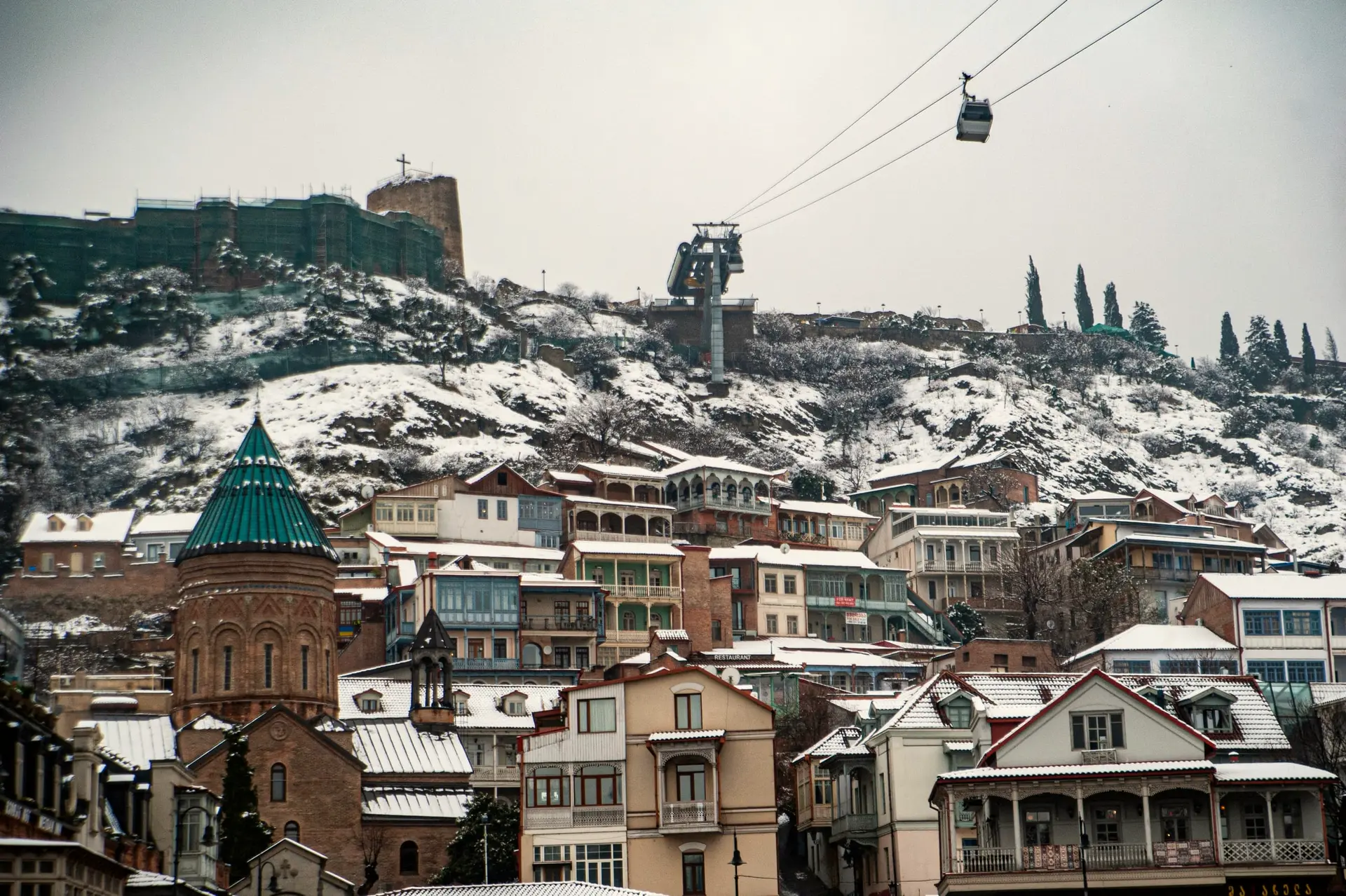 Old Tbilisi under snow, with Narikala fortress and the cable car above the roofs